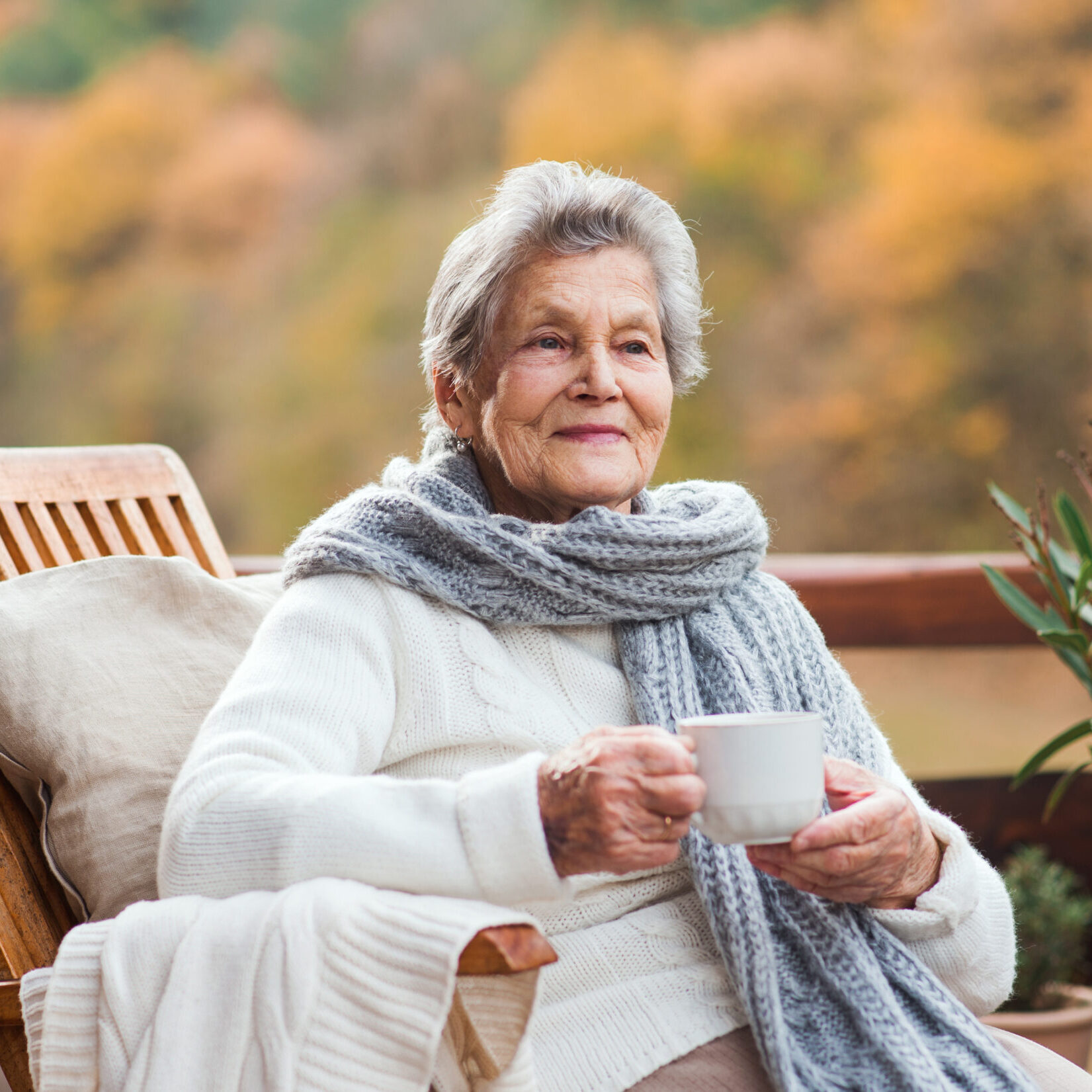 An elderly senior woman sitting outdoors on a terrace in on a sunny day in autumn.