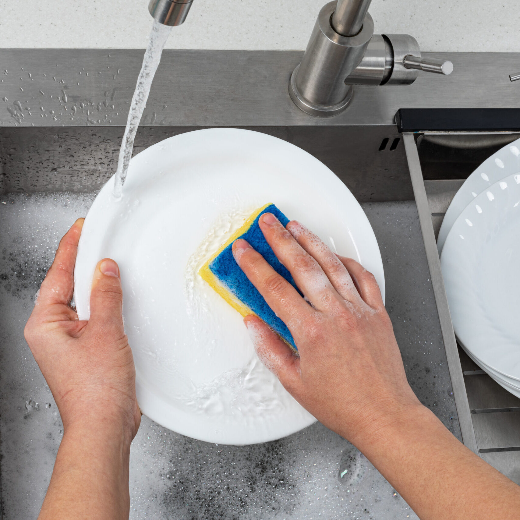 Different clean dishware, cutlery and glasses on countertop near sink in kitchen